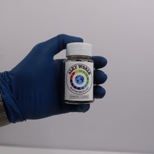 Hand wearing a blue glove holding a small jar  of Charcoal Capsules with a colorful label against a plain background