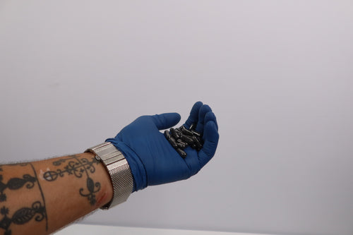 Hand wearing a blue glove holding Charcoal Cleansing Capsules against a plain background