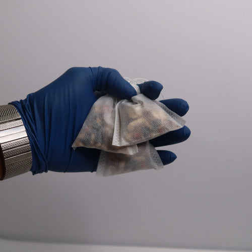 Hand wearing a blue glove holding transparent bags with contents against a gray background