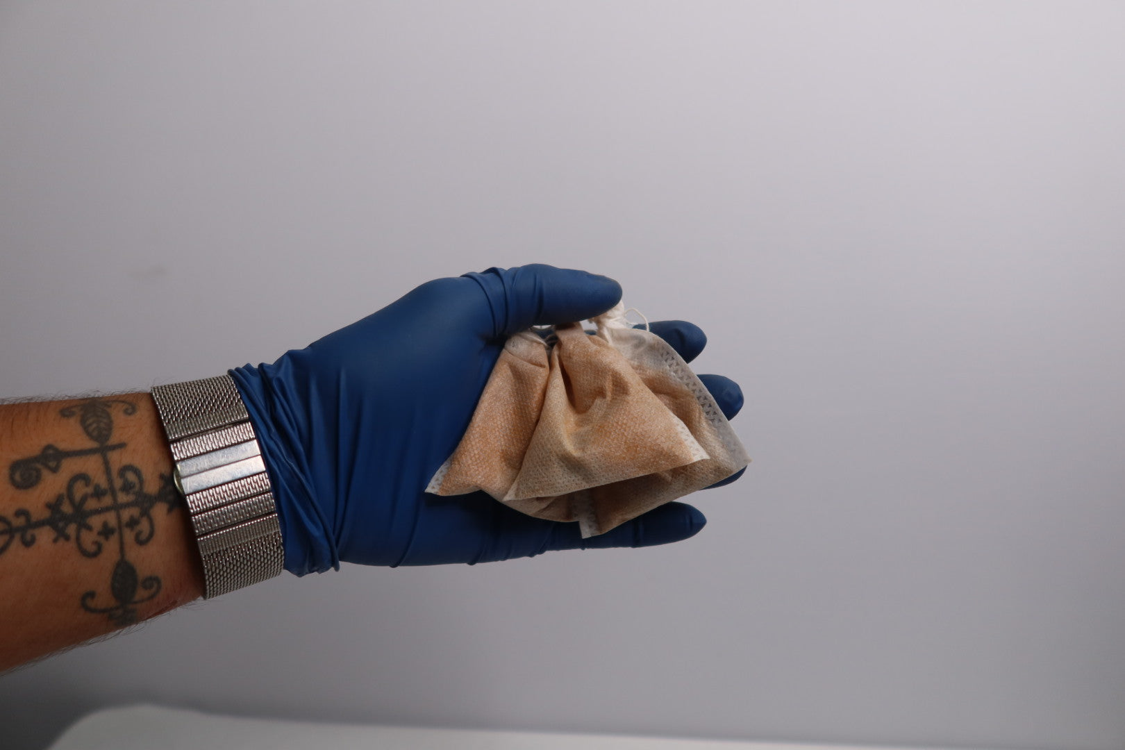Hand wearing a blue glove holding a brown paper bag against a gray background